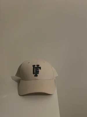 Beige keps med svart broderad logga - Snygg beige keps med böjd skärm och svart broderad LF-logga framtill. 
