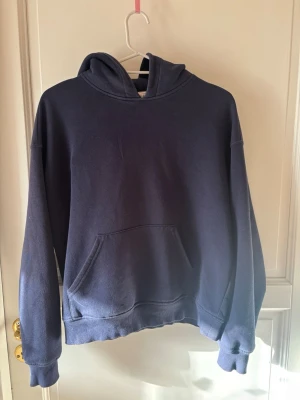 Mörkblå hoodie med ficka - En enkel och stilren mörkblå hoodie med huva och stor magficka. Hoodien har ribbade muddar vid ärmslut och nederkant, perfekt för en avslappnad och bekväm look. Passar till jeans eller mjukisbyxor.