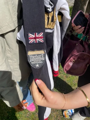 Svart och vit hoodie från Lonsdale - Cool hoodie från Lonsdale i svart och vitt med röda detaljer. Stor logga och lejon på bröstet, Union Jack-flagga och patch på ärmen. Jätte bra pris värsting huligan hoodien bra å ha på matcher 