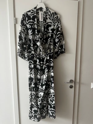 Svartvit långklänning från Kappahl - Snygg långklänning från Kappahl med svartvitt blommigt mönster. Klänningen har vida trekvartsärmar. Aldrig använd, prislapp kvar. Skicka gärna prisförslag. Skickar omgående 
