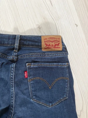 Blå bootcut jeans från Levi's - Snygga blå bootcut jeans från Levi's med klassisk femficksdesign och ikonisk röd etikett på bakfickan. Jeansen har en något utsvängd passform och slitna detaljer vid benslut. Perfekta för en avslappnad och trendig look.