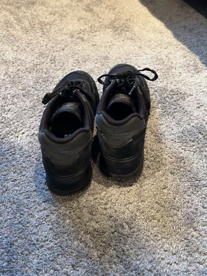 Svarta New Balance 574 sneakers - Snygga svarta New Balance 574 sneakers med klassisk siluett. Skorna har ovandel i textil och mocka, samt detaljer i läder. Tjock sula för extra komfort och snörning framtill. Perfekta för en sportig och stilren look.