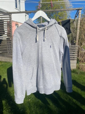 Grå hoodie från Polo Ralph Lauren - En lite schysstare hoodie från Ralph Lauren! Hoodien är HELT oanvänd och i perfekt skick. Den var tyvärr för liten för mig så därför säljer jag den. Stilren, klassisk och passar till allt. Perfekt för sena sommarkvällar☀️ Tveka inte med att ställa frågor!🤗⭐️   Mått utefter sista bilden:  Axel till midja: 62cm Midja: 46cm Armlängd: 70cm