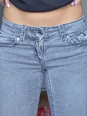 Ljusgrå low waist jeans - Säljer ett par ljusgrå low waist jeans med raka ben och snygga fickdetaljer bak. Jeansen har klassisk femficksdesign, silverfärgade knappar och dragkedja. Materialet är stretchigt denim som sitter skönt och formar sig efter kroppen.