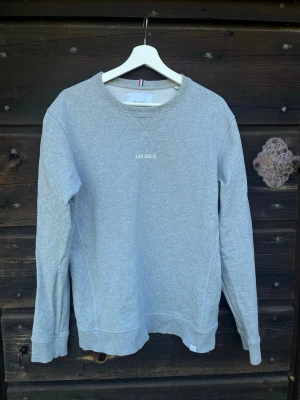 Grå sweatshirt från Les Deux - Klassisk grå sweatshirt från Les Deux med rund halsringning och diskret logotyp broderad på bröstet. Tröjan har ribbade muddar vid ärmslut och nederkant samt är gjord av bomull som gör den riktigt skön att bära.