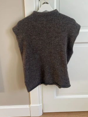 Mörkgrå ärmlös stickad tröja  - Säljer en mörkgrå ärmlös stickad tröja i mjukt material. Tröjan har hög hals och rak passform, perfekt att bära över en skjorta eller t-shirt. Enkel och stilren design som passar till många olika outfits. Från Gina tricot, storlek L men passar mig som är xs-S