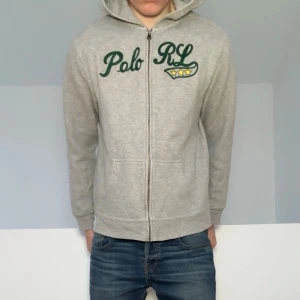 Grå Ralph Lauren zip hoodie - Säljer en sjukt fet zip hoodie från Ralph Lauren. Hoodien är i bra skick utan nåra defekter och är färgen ljusgrå. Den är i strl 18-20 vilket motsvarar ungefär strl S! Hör gärna av er vid frågor elr funderingar!!