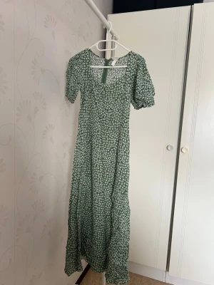 Grön blommig långklänning med puffärm - Grön långklänning med vitt blommönster och puffärmar. Klänningen har söt uringnig och en slit framtil. Perfekt för dig som gillar romantisk och trendig stil. Skriv för fler bilder och frågor❤️säljer då de inte passar mig 