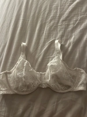 Vit spets-bh  - Elegant vit bh med bygel och tunna axelband. Bh:n är tillverkad i genomskinlig spets med blommigt mönster och har en klassisk form som ger bra stöd. Perfekt för dig som gillar romantiska detaljer och en feminin look.