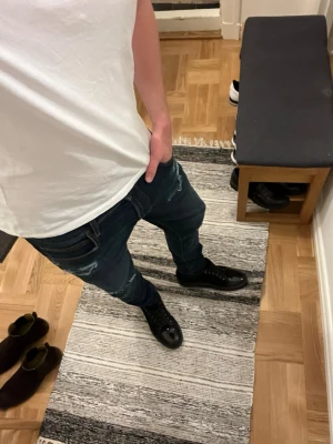Mörkblå Lee jeans med slitningar - Säljer ett par mörkblå slim jeans med slitningar och distressed detaljer på både lår och knän. Jeansen har klassisk femficksmodell och tapered passform. Perfekta för en avslappnad och trendig look. 