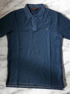 Marlboro piké  - Klassisk blå pikétröja från mcs med korta ärmar och krage. Tröjan har en liten gul broderad logga på bröstet och knäppning vid halsen. Tillverkad i mjuk bomull som känns skön mot huden. Perfekt för en avslappnad och stilren look. Använd knappast 1 gång då jag skaffade den i slutet av sommarn. Skriv gärna vid frågor och priset går att diskutera