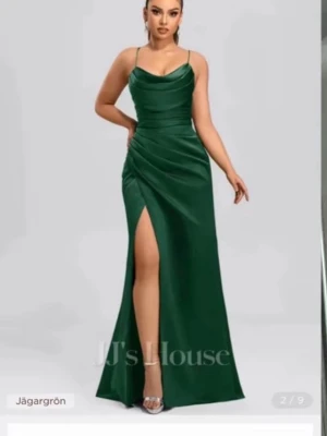 Grön långklänning med slits JJ's House - Elegant långklänning i djup grön färg från JJ's House. Klänningen har smala axelband, snörning i ryggen och en hög slits framtill. Materialet har en satinliknande finish som ger en lyxig känsla. Perfekt för speciella tillfällen.
