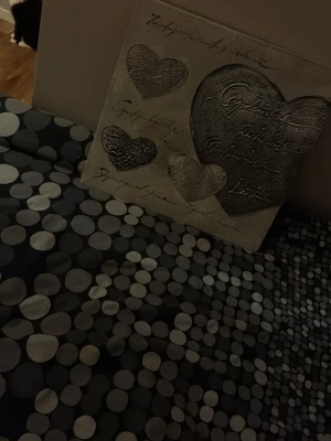 Tavla med hjärtan och text - Säljer en fyrkantig tavla i vitt och silver med flera hjärtan i relief och dekorativ text. Tavlan har en romantisk och konstnärlig stil, perfekt som inredningsdetalj till sovrum eller vardagsrum.