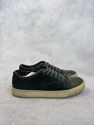 Mörkgröna Lanvin sneakers med mocka och läder - Snygga mörkgröna sneakers med ovandel i mocka och tåparti i blankt läder. Skorna har grå skosnören och en vit, något sliten sula. Perfekta för dig som gillar en stilren och klassisk look med en twist.