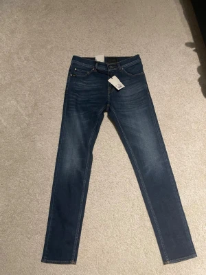 Tiger of Sweden blå jeans Evolve 28/32 - Säljer dessa nya mörkblåa jeans från Tiger of Sweden, modell Evolve. De har klassisk femficksdesign, smal passform och raka ben. Jeansen är tillverkade i bomull med en mörk tvätt och subtila slitningar framtill. Perfekt för dig som gillar stilrena och moderna jeans.