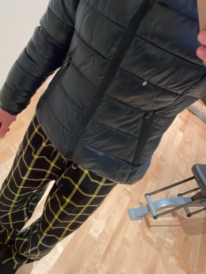 Svart/blå dunjacka med huva - Säljer en svart dunjacka med huva och dragkedja framtill. Jackan har två sidofickor med dragkedja och quiltad design. Perfekt för kalla vinterdagar och riktigt skön att ha på sig. De är en nikki pufferjacket från lager 157!