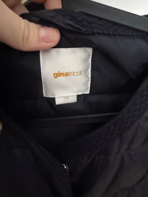 Mörkblå pufferjacka från Gina Tricot - Snygg mörkblå pufferjacka från Gina Tricot med rund halsringning och tryckknappar framtill. Jackan har två framfickor och quiltad design som ger en cool look. Perfekt för kalla dagar och enkel att matcha med olika outfits.