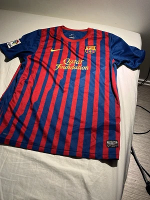 Barcelona matchtröja Nike röd/blå - Säljer en FC Barcelona matchtröja från Nike med klassiska röda och blå vertikala ränder. Tröjan har Qatar Foundation- och UNICEF-loggor samt klubbmärke på bröstet. Korta ärmar och sportig passform, perfekt för fotbollsträning eller att bära till vardags.