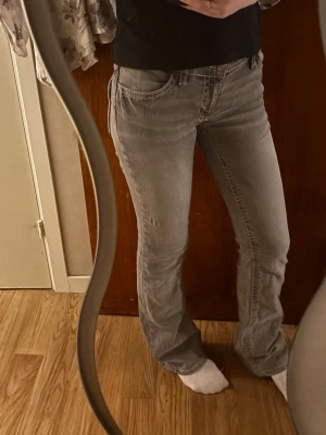 Grå bootcut jeans - Säljer ett par grå bootcut jeans med vita sömmar och snygga detaljer på bakfickorna. Jeansen har normal passform och klassisk femficksdesign. Storlek 170