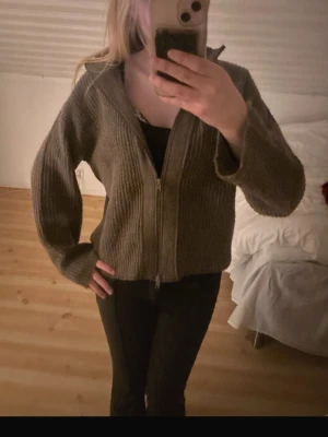 Brun stickad kofta med dragkedja - Mysig brun stickad kofta med lång ärm och dragkedja framtill. Koftan har en loose passform och är perfekt för kyliga dagar. Ribbad struktur och hög krage ger en chill och avslappnad vibe. Passar dig som gillar enkla och bekväma plagg.