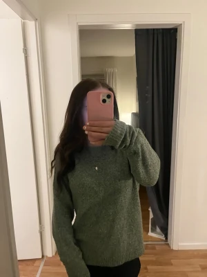 Grön stickad tröja  - Mysig stickad tröja i en dov grön färg med avslappnad, oversize passform. Tröjan har rund halsringning och långa ärmar med ribbstickade muddar. Perfekt för lager-på-lager och chill dagar. Materialet känns mjukt och värmande.