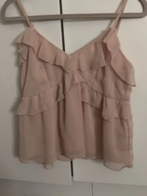 Ljusrosa volang-linnetopp - Supersöt ljusrosa linnetopp från Nelly med volangdetaljer och tunna axelband.🥹🙏🏼💗 Toppen är luftig och har en romantisk känsla, perfekt för varma dagar. Materialet är tunt och lätt, perfekt om du vill vara finklädd men inte alldeles för fancy. Använd ett par gånger bara! 💓💗 Skriv privat ifall du skulle vilja se den bättre eller någon övrig information. Pris kan diskuteras