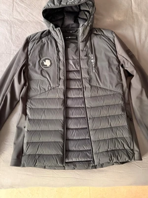 Svart pufferjacka från Sail Racing  - Säljer en svart pufferjacka från Sail Racing. Perfekt för kalla höst/sommardagar och riktigt stilren design. Muddarna är trasiga/saknas. En skräddare kan säkert rädda jackan eller gör om den till en schysst väst?. I övrigt fint skick. 