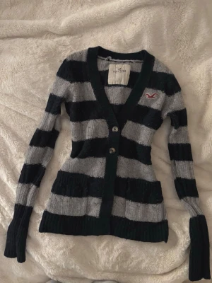 vintage yk2 hollister stickad kofta/topp - så fin ikonisk vintage stickad långärmad från hollister i stl S💗 den är mörkblå/grå randig, har två fickor där fram och djup urringning. lite nopprig vilket man kan se på bilden men övrigt fint skick för sin ålder! 