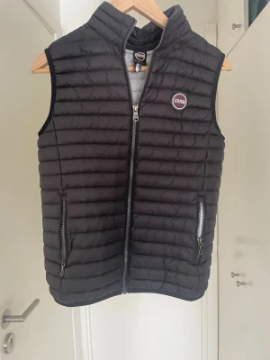 Svart dunväst från Colmar - Säljer denna Snygga svarta dunvästen ifrån comlmar. Västen är i ett fint sick men har en lagning som ni ser på den sista bilden. Storlek : 14 år/ 166 cm