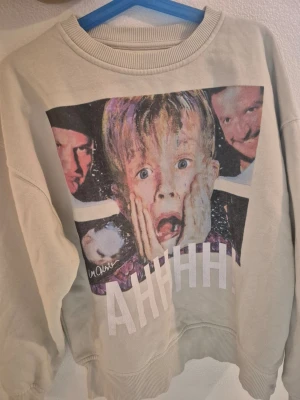 Barn Beige sweatshirt med filmtryck storlek 134  - Cool beige sweatshirt med stort färgglatt tryck från filmen Ensam Hemma och texten 'AHHHH!' framtill. Tröjan har rund halsringning och ribbade muddar vid ärmslut och nederkant. Perfekt för dig som gillar filmklassiker och vill sticka ut. Har du tvillingar passar på ta hela paketet för 220sek