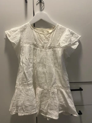 Vit blus med volang från Gina Tricot - Söt vit blus från Gina Tricot med volangdetaljer och korta ärmar. Perfekt till jeans eller kjol för en fräsch look. Rund halsringning och fina sömmar som ger extra stil.