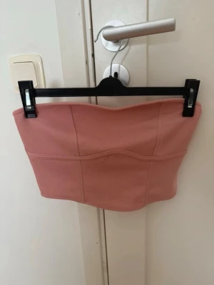 Rosa bandeau tubtopp - Säljer en snygg rosa bandeau tubtopp med markerade sömmar och en stilren, croppad passform. 