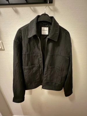 Svart overshirt från Bershka - Säljer en svart overshirt från Bershka med strukturerat tyg och två stora fickor framtill. Jackan har dragkedja och en klassisk krage. Perfekt att slänga över en hoodie eller t-shirt. Använt väldigt få gånger, som ny. 