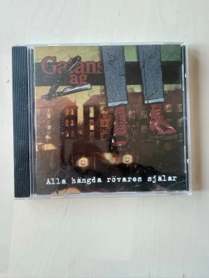 CD Gatans lag  - Alla hängda rövares själar - CD-skiva med albumet 'Alla hängda rövares själar' . Omslaget har illustration av ben med röda skor mot en bakgrund av mörka byggnader. Baksidan listar 18 låtar och har logotyp för PST Records.