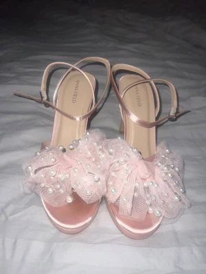 Rosa pumps med pärlor från Anna Field - Snygga rosa pumps med hög klack från Anna Field. Skorna har rem runt ankeln och är dekorerade med stora tyllrosetter och vita pärlor framtill! Bekväma, aldrig använda bara testade! Storlek 41 men passar även 42