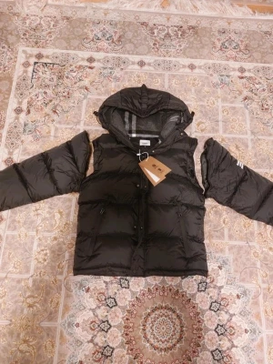 Svart o vitt Bụrberrŷ - Snygg svart dunjacka från Bụrberrŷ med stor vadderad huva och dragkedja framtill. Jackan har två sidofickor med dragkedja och Off-White-logga på ärmen. Perfekt för kalla dagar och riktigt trendig look.