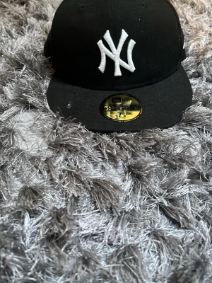Svart New Era Yankees keps - Säljer en svart New Era 59FIFTY keps med klassiskt New York Yankees broderat vitt logotyp framtill och MLB-logga bak. Rak skärm och stilren design, perfekt för dig som gillar streetwear och sportig stil.