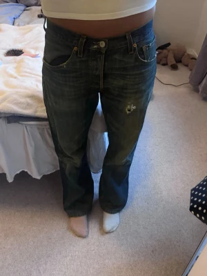 Levi's jeans - Baggy blå jeans från Levi's med klassisk femficksdesign och låg midja. Jeansen har en avslappnad passform och slitningar på låret samt en liten broderad detalj på ena benet. Perfekta för en chill och trendig look.