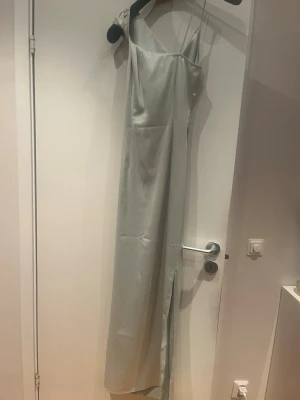 Ljus grön klänning från adoore  - Elegant ljusgrön  långklänning med en axelbandslös design och smal passform. Klänningen har en stilren slits framtill och är tillverkad i ett glansigt material som ger en lyxig känsla. Perfekt för dig som ska på bal eller gå på bröllop  Endast använd en gång på balen men har inga fläckar eller är sönder utan sparsamt använd 