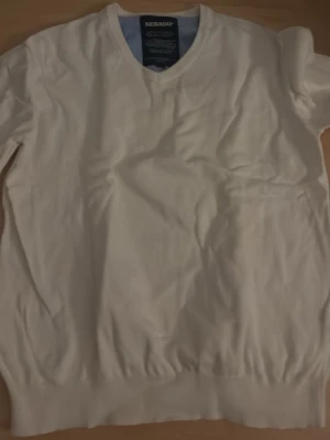 Vit stickad tröja från Sebago - Klassisk vit stickad tröja från Sebago med rund halsringning och ribbade muddar vid ärmslut och nederkant. Tröjan har en enkel och stilren design som passar till många olika outfits. Tillverkad i mjukt material för extra komfort. Sitter som M