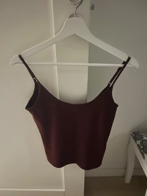 Vinröd linnetopp med smala band - Snygg vinröd linnetopp med smala axelband och enkel, croppad passform. Perfekt att styla till jeans eller kjol för en trendig look. Materialet känns mjukt och stretchigt, vilket gör toppen bekväm att bära.