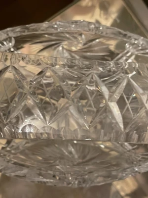 Rund kristallskål med slipat mönster - Säljer en rund kristallskål med vackert slipat mönster och dekorativa stjärn- och diamantformer. Skålen är genomskinlig och har en tjock kant med detaljerade snitt. Perfekt som dekoration eller för servering av godis eller snacks.