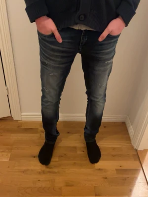 Mörkblå slim fit jeans med slitningar - Snygga mörkblå slim fit jeans med lätt slitna detaljer och tvättade partier. Jeansen har klassisk femficksdesign och smal passform som sitter tajt längs benen. Perfekta för en trendig och avslappnad look.