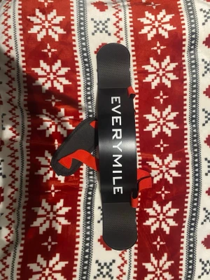 Everymile armblaster för gymträning - Säljer en svart armblaster från EVERYMILE med röda justerbara remmar och vadderad nackdel. Perfekt för att isolera biceps under styrketräning. Tillverkad i metall och nylon med tydlig logga framtill.