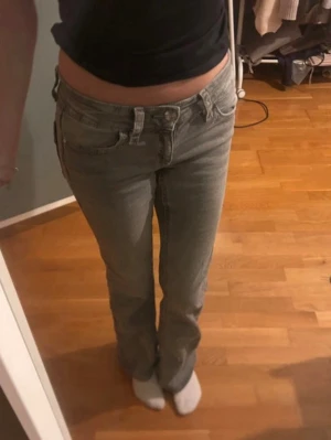 Grå bootcut jeans med fickdetaljer - Säljer ett par grå bootcut jeans med låg midja och snygga fickdetaljer bak. Jeansen har klassisk femficksdesign och är i ett mjukt denimtyg. Perfekta för dig som gillar en avslappnad men trendig look.