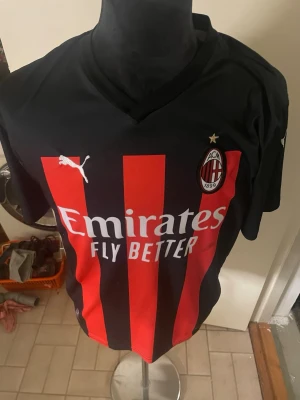 AC Milan Ibrahimović matchtröja - Snygg AC Milan matchtröja från Puma med Ibrahimović och nummer 11 på ryggen. Tröjan är svart med röda vertikala ränder, klubbmärke och Puma-logga på bröstet samt Emirates Fly Better-tryck. Korta ärmar och officiella Serie A-märket på ärmen.Finns nån fläck på tröjan vid sponsoren 