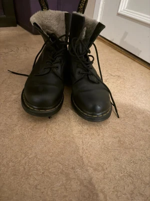 Svarta Dr. Martens kängor med foder - Säljer ett par svarta Dr. Martens kängor med snörning och varmt, ljust foder. Klassisk gul söm runt sulan och dragflik bak. Perfekta för kalla dagar och ger en cool stil till vilken outfit som helst.