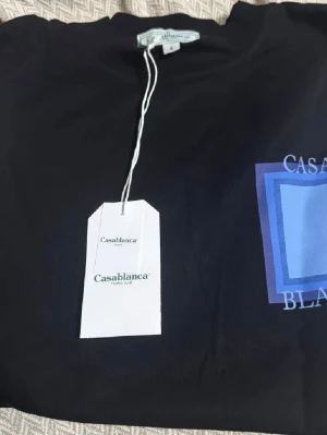 Svart Casablanca t-shirt med tryck - Casablanca t-shirt i svart med ett stort grafiskt tryck i blå och vita toner på bröstet. Klassisk passform och rund hals. Tillverkad i mjuk bomull och har en stilren look med logotypdetaljer framtill. Pris kan diskuteras 