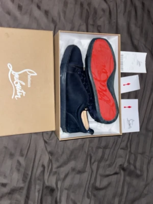 Blåa sneakers från Christian Louboutin - Snygga blåa sneakers från Christian Louboutin i mocka med klassiska röda sulor. Skorna har blå skosnören, metallöljetter och låg profil. Perfekta för dig som vill ha en exklusiv och stilren look med en ikonisk touch.