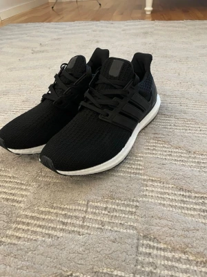 Svarta Adidas Ultraboost sneakers - Säljer ett par svarta Adidas Ultraboost sneakers med vit sula och svart ovandel i mesh. Skorna har snörning, Torsion System och Continental-gummisula för extra grepp. Perfekta för dig som vill ha både stil och komfort till vardags eller träning.helt nya